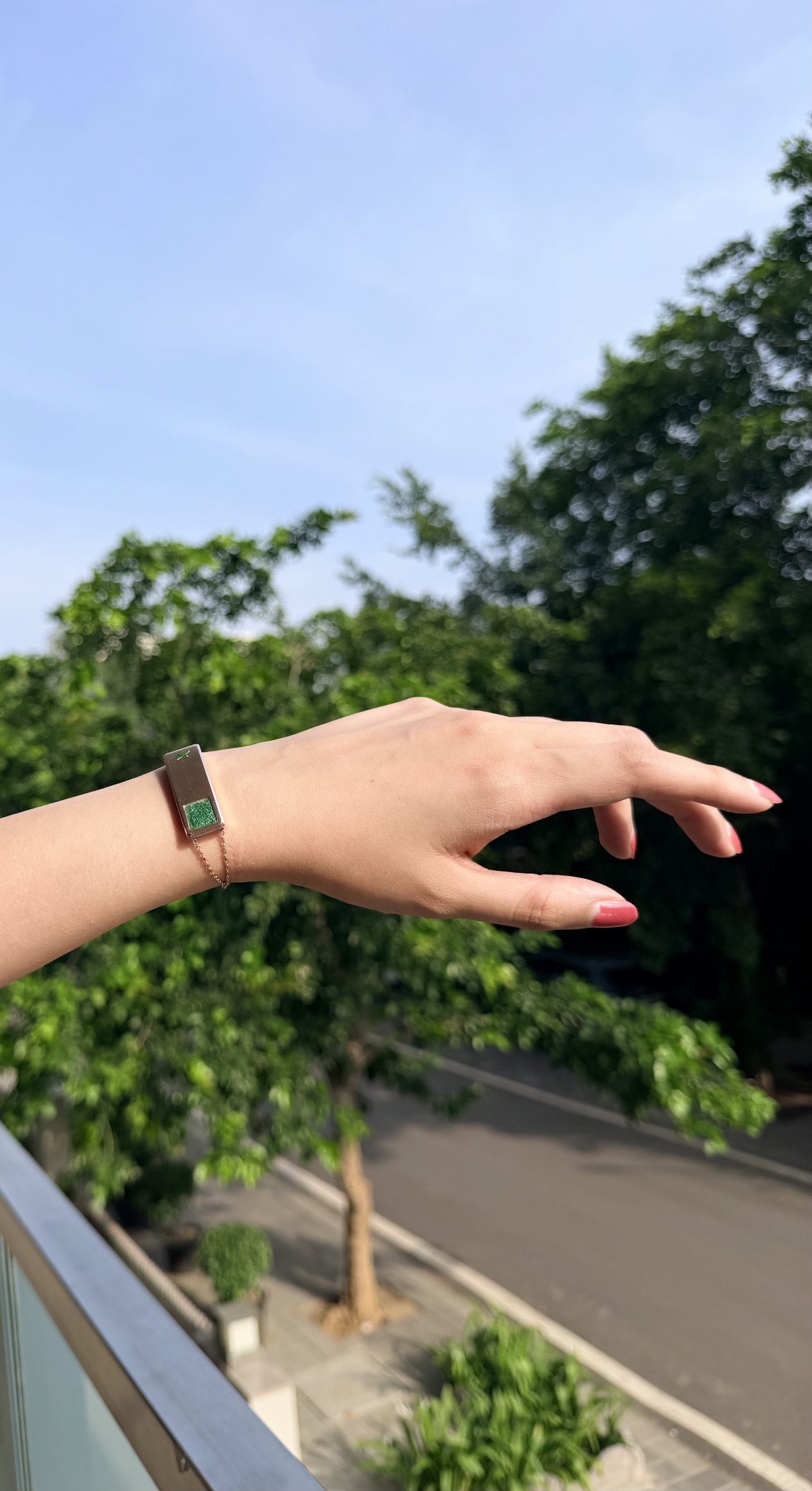 A woman's hand wearing the Puzzl steel bracelet against open sky and trees
